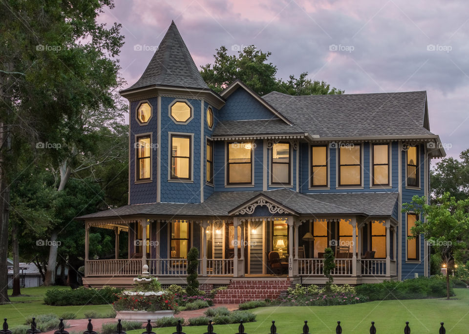 eerie yet beautiful image of a Victorian style home with a golden glow in the windows against a background of pink and blue clouds