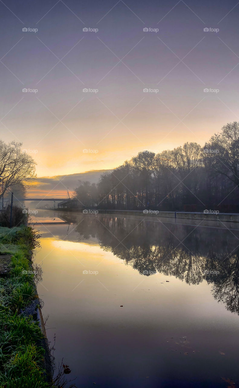Glowing sunrise or sunset over the water of a river or canal flowing through a forest landscape