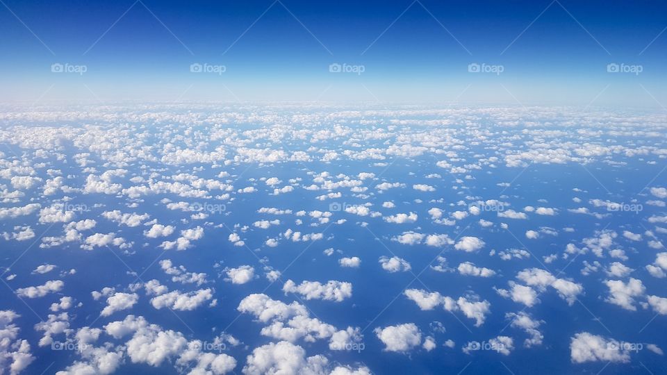 Airplane view of ocean and blue sky with lots of small white clouds in fair weather - utsikt från flygplan över blått hav och blå himmel med många små vita moln 