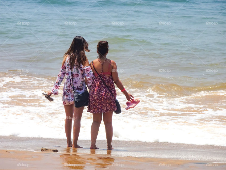 two woman holding hands standing inside sea water on the beach in summer