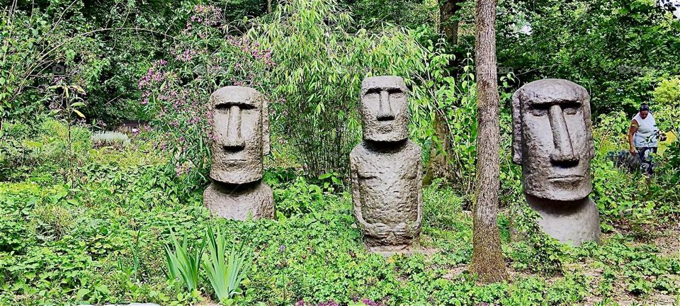 These primitive stone statues of men are on display at “Himalaya Nepal Park” in “Wiesent”, “Bavaria”, Germany looking out at us from the lush green vegetation. 2024. Hypnotic Productions