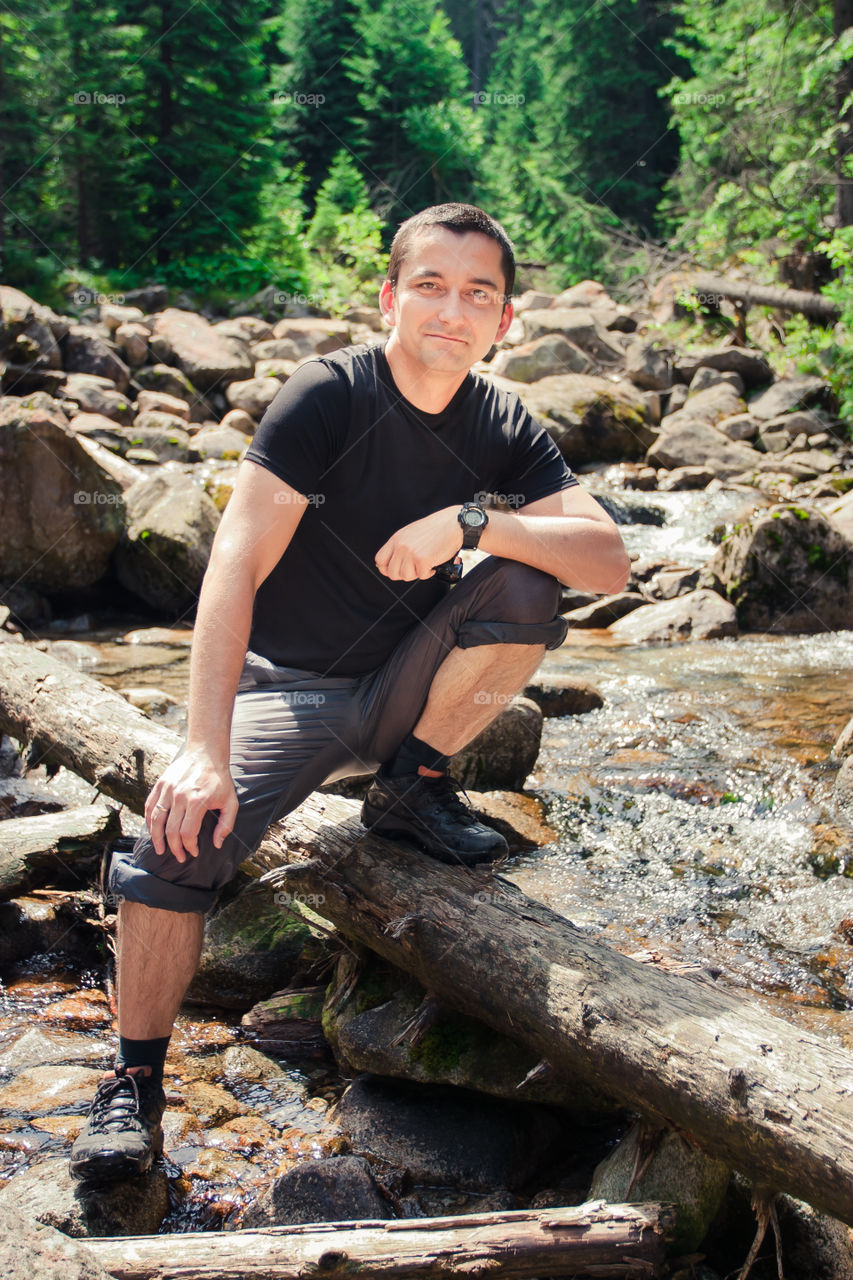 Man sitting by the stream. Man sitting on trunk on mountain trail