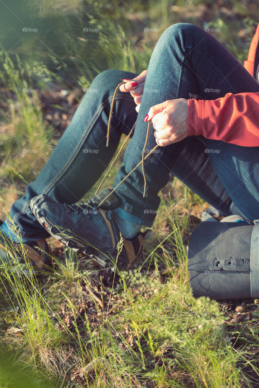 Young woman hiker with backpack taking a shoe off to put a plaster aid on her foot due to tight shoe during summer vacation trip in forest