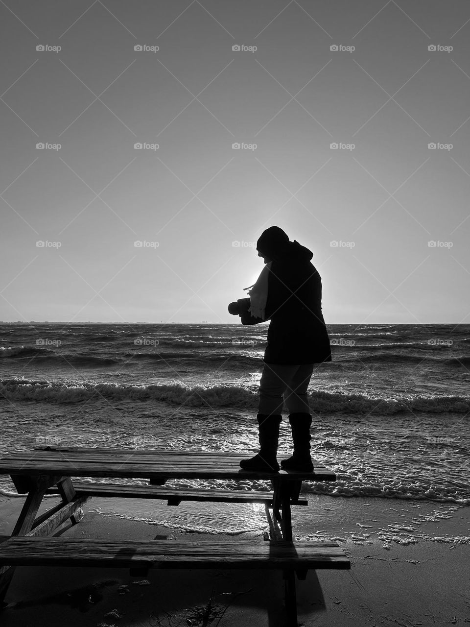 Climate Change Before/After Photo - A photographer stands on a picnic table and captures waves crashing onto the beach front. Tornado winds causing havoc on and eroding the military campground. 