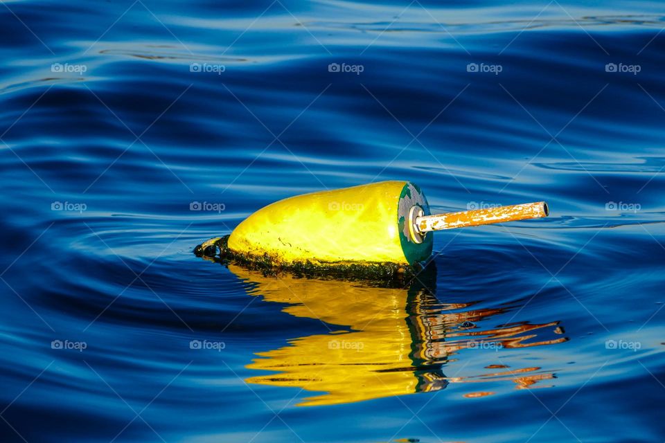 A yellow buoy drifts among the deep blue of the ocean.