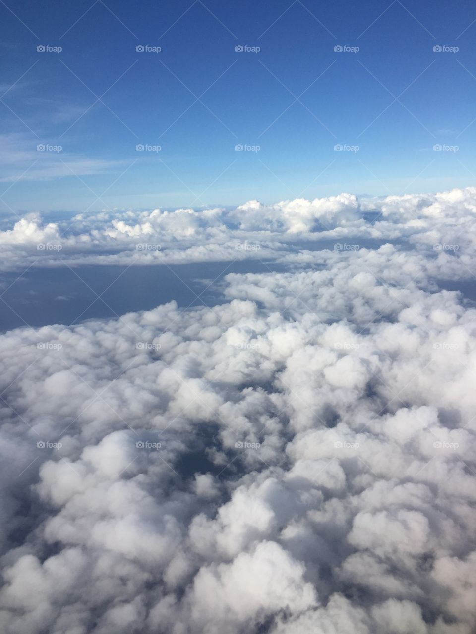 Photo of the sky white fluffy clouds and dark blue ocean below, taken from an airplane.