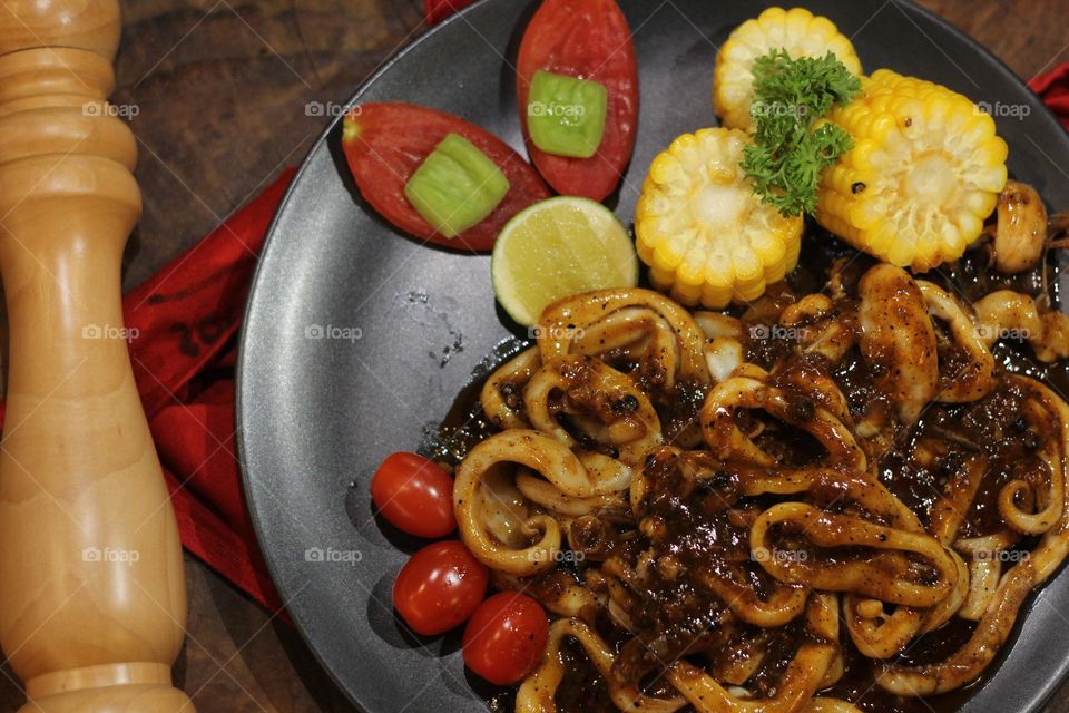 Close-up portrait of squid rings seasoned with barbecue sauce served on a black plate on a wooden table, wooden barbecue spice shaker background — Stock Photo