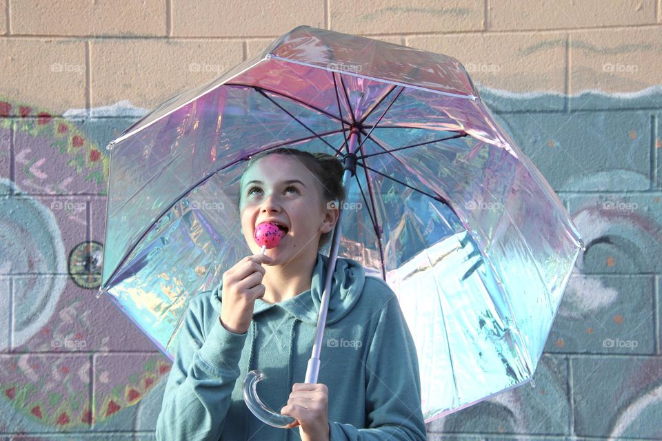 Girl with lollipop holding blue iridescent umbrella with baby blue background      