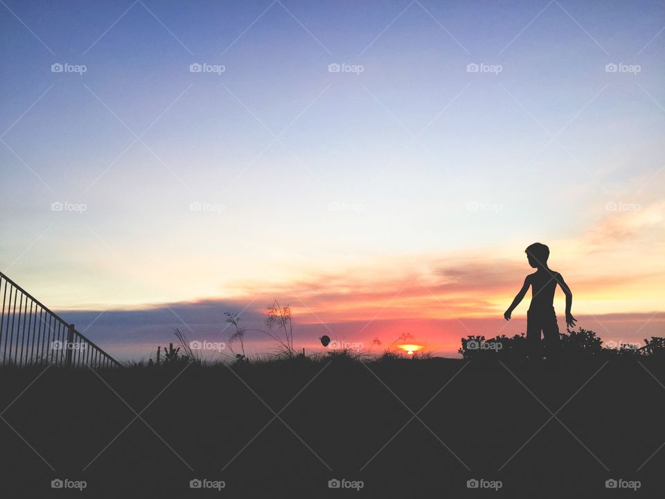 Boy stands against a purple sky ready to catch a baseball. 