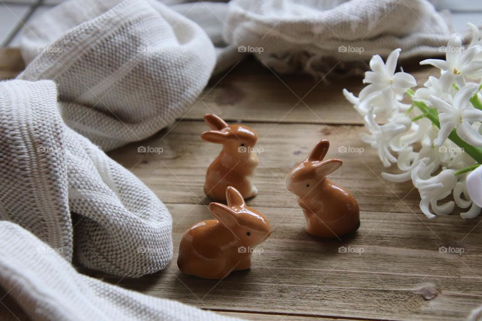 Year of the rabbit. 3 ceramic rabbits on wooden background with flowers and cloth.