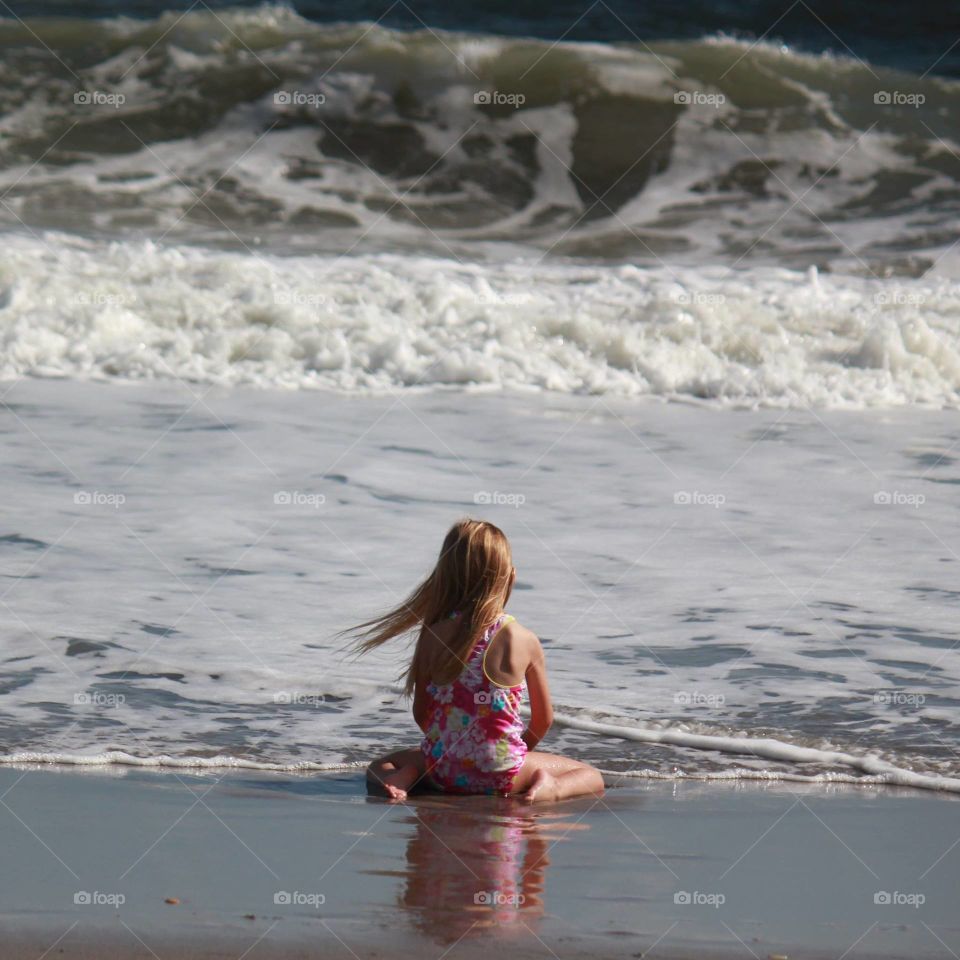 Little girl sitting at the shore of the beach 