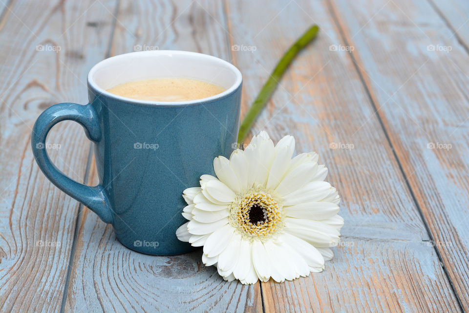 blue cup of coffee on a wooden table  background with a white daisy flower decoration