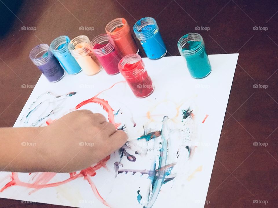Young child is painting and creating a piece of artwork using bold, vivid and bright finger paints 