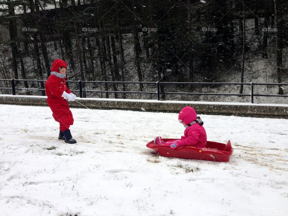children playing in the snow and pushing a sledge