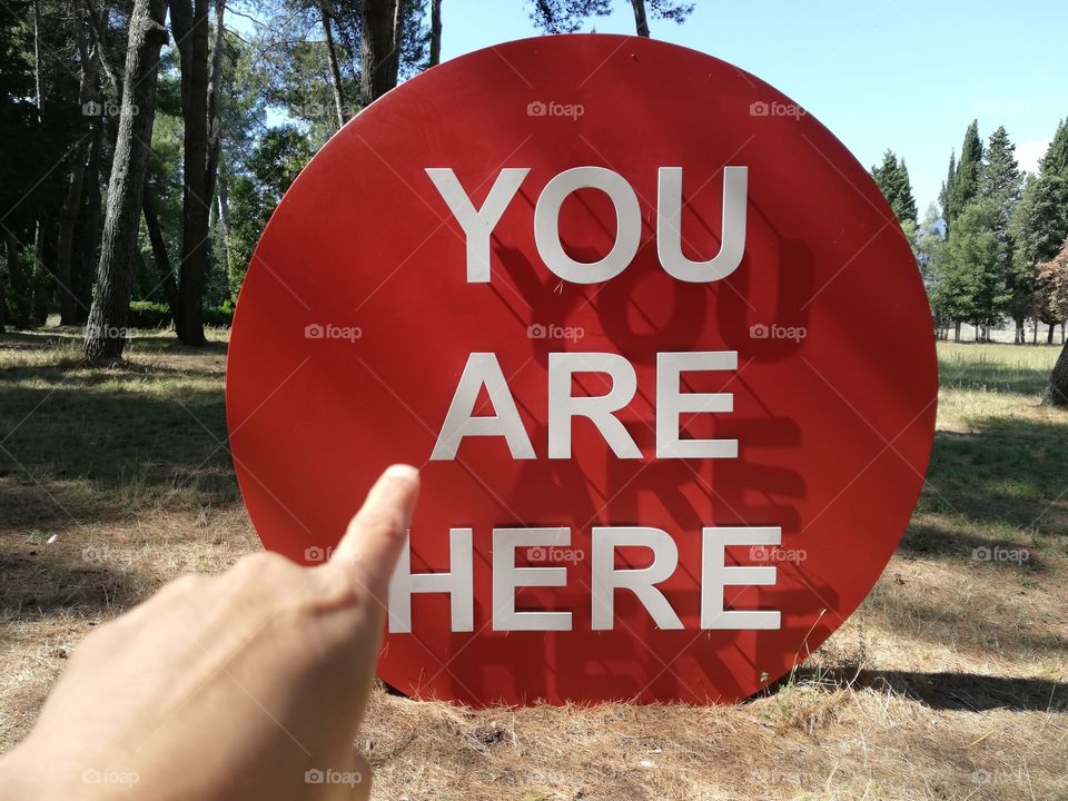 Finger points to red sign with writing: you are here