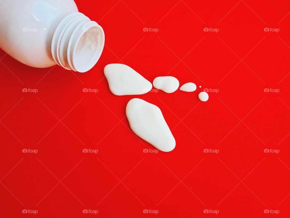 drops of milk falling from the overturned bottle on a red background