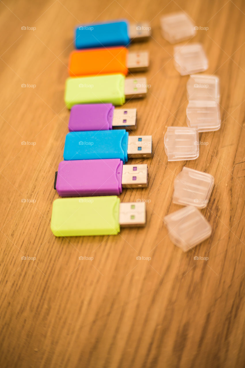 Multi-colored flash drives for working with documents, saving and transmitting, sharing files on a wooden texture table close-up.