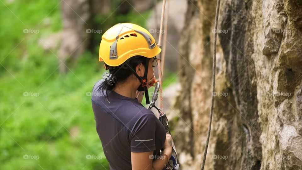 Close-up of young female rock climber in action. He wore a yellow helmet and other safety equipment