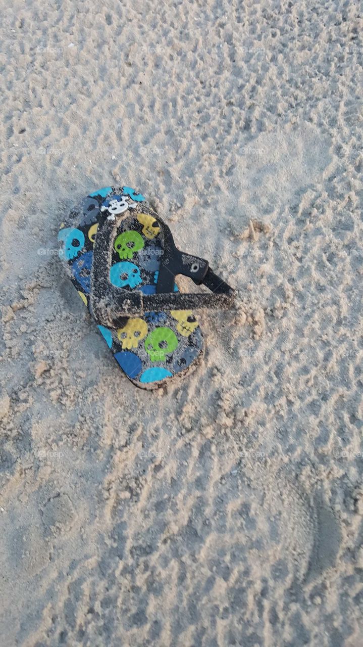 An abandoned child's sandal lays alone on a sandy summer beach.