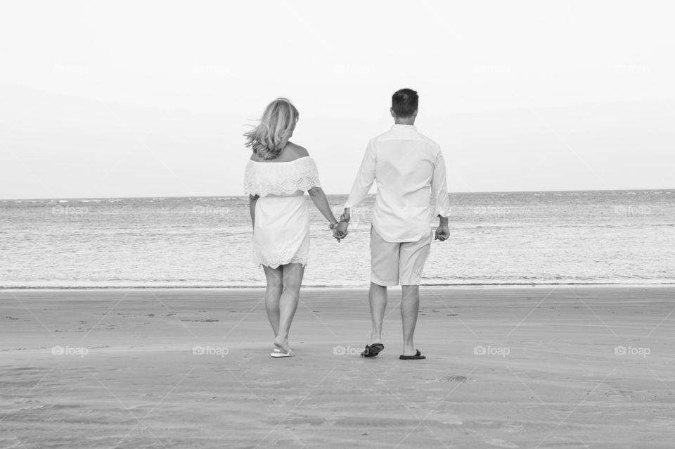 Black and white back view of a couple holding hands and walking along the beach