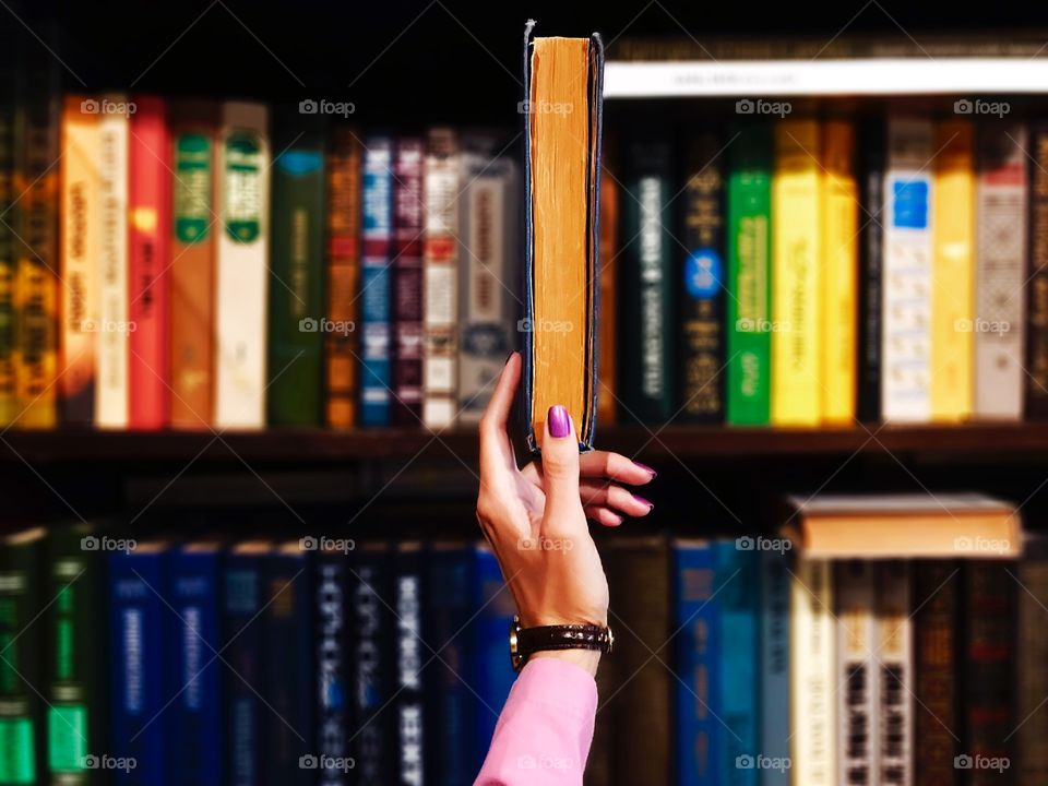 Female hand taking an old book from the bookshelf with lots of old colorful books in the bookstore or library 