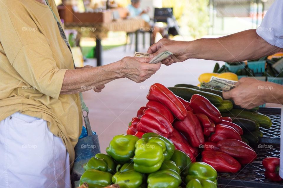 Woman buys vegetables at farmers market in summer with cash to purchase it in this exchange for food