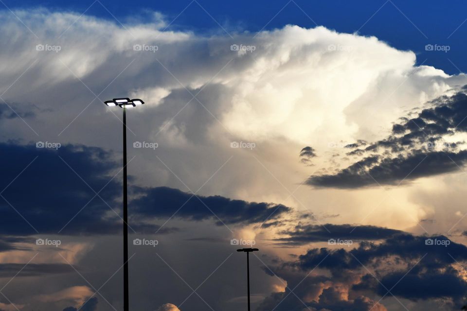 Mountainous clouds moving with a storm front completely engulf a parking lot leaving with the street lights left standing.