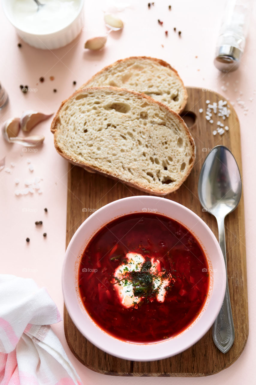 Polish red borscht soup in pink bowl with sour cream, bread, garlic and spices on pink background. Top view. Flat lay