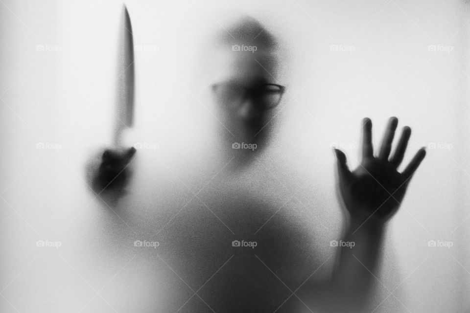 Horror Murderer. Dangerous man behind the frosted glass with a knife on his hand.Halloween background.Black and white picture
