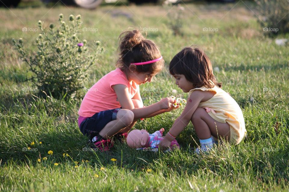 Two cute girls are playing with dolls on a soccer field