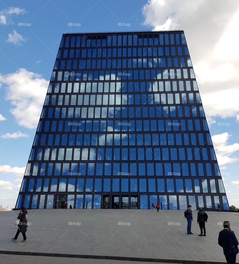 Reflection of clouds on glass facade of building with modern architecture with bright sky with clouds behind