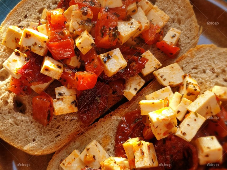 Close-up of two slices of bread with a spread of tomatoes, tofu and herbs.