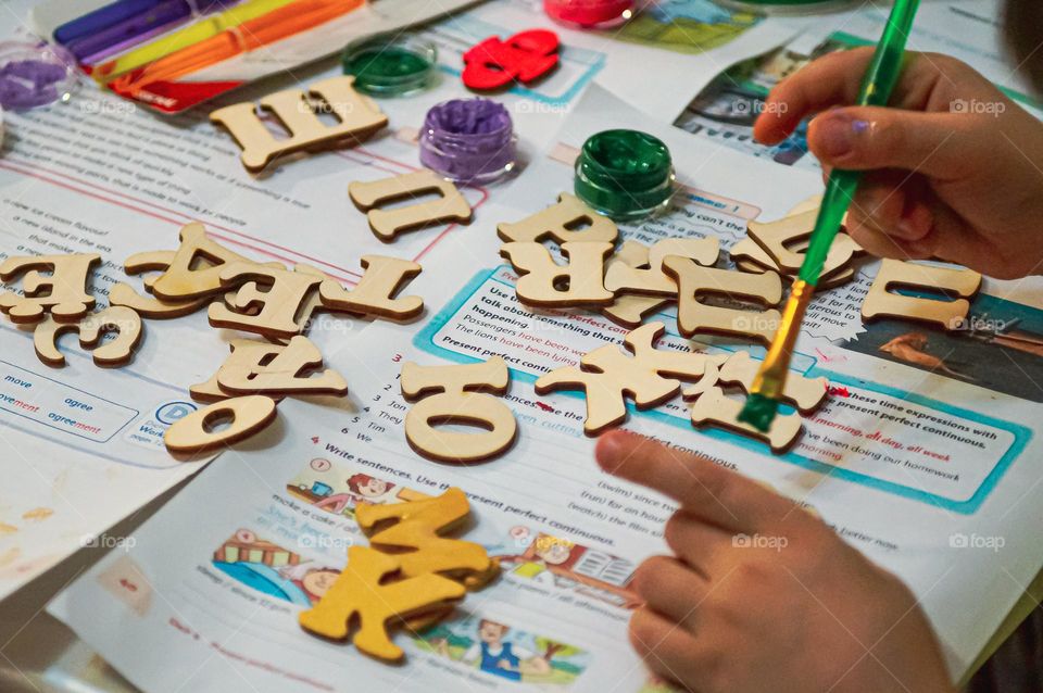 The boy paints wooden letters in different colors