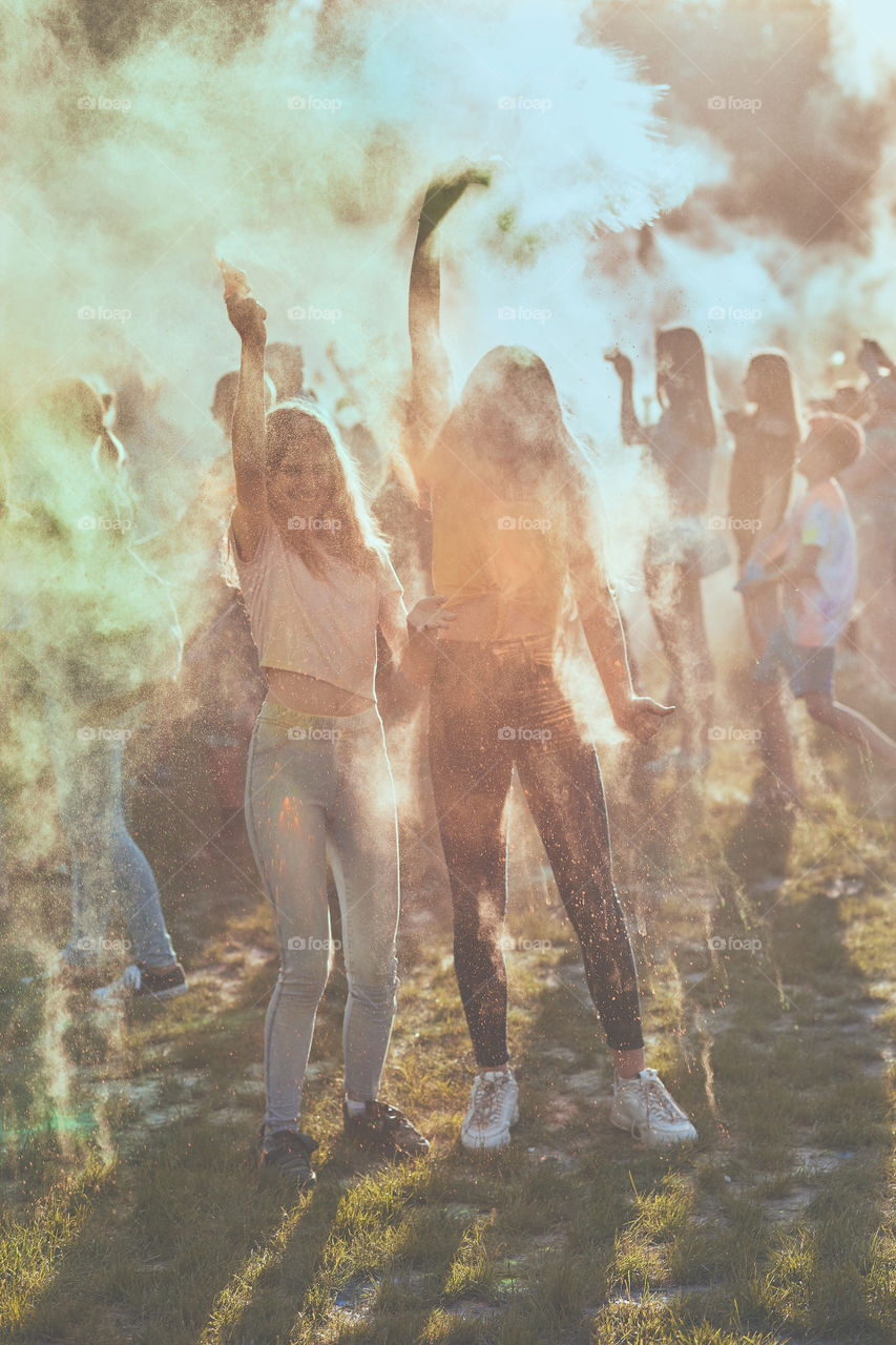 Portrait of happy smiling young girls with colorful paints on faces and clothes. Two friends spending time on holi color festival. Real people, authentic situations