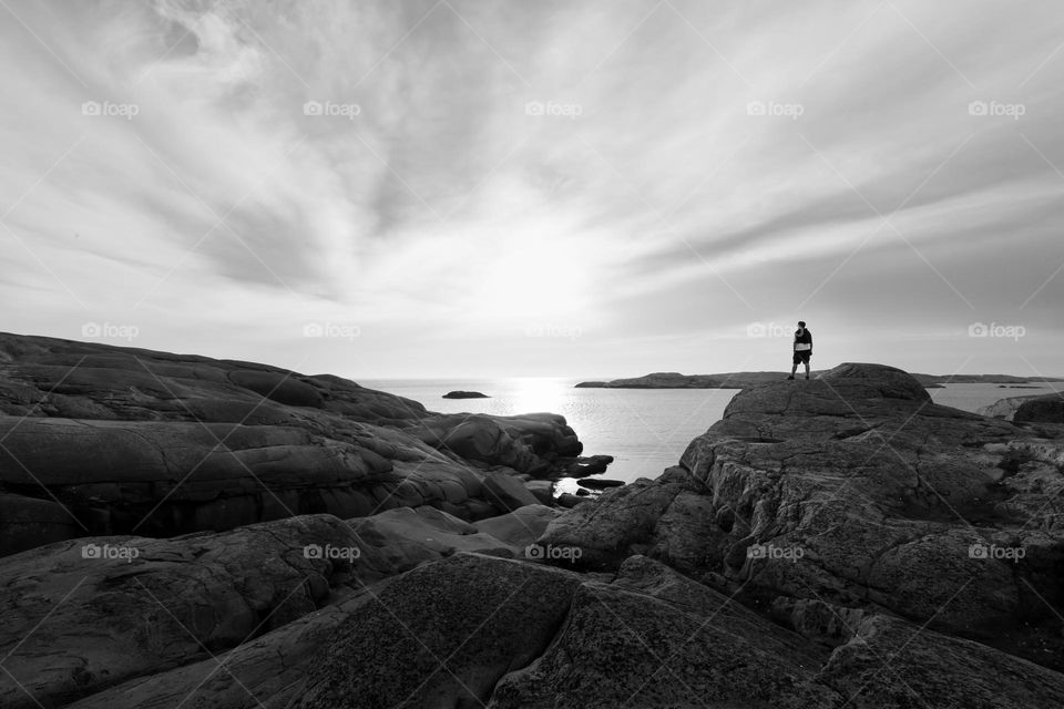Man standing alone on the cliffs by the ocean watching a beautiful sunset, b&w