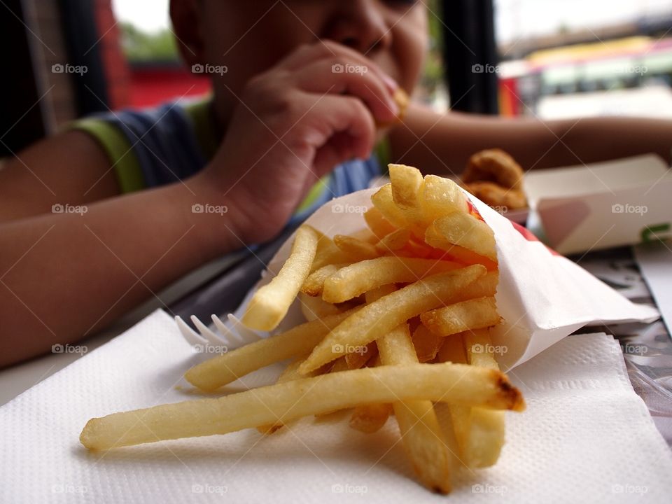 french fries and a boy eating in the background