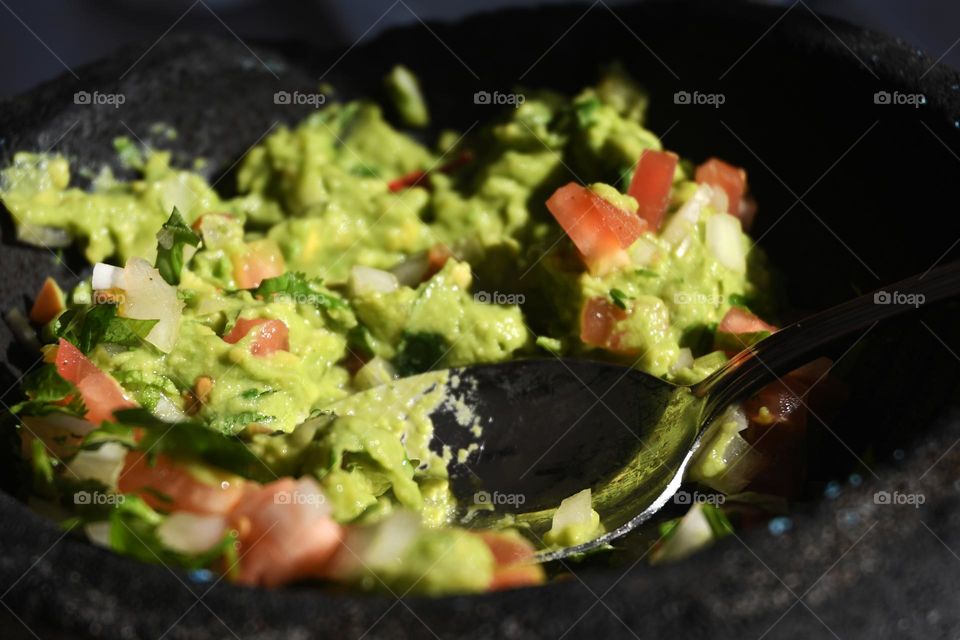 A spoon sits in a bowl of freshly homemade guacamole dip filled with diced tomatoes.