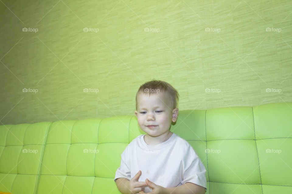 A portrait of a child sitting at home on a green sofa depicts different emotions in yellow shorts.