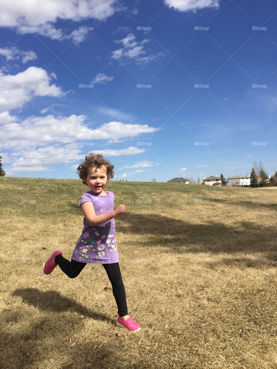 Curly haired girl running down grassy hill