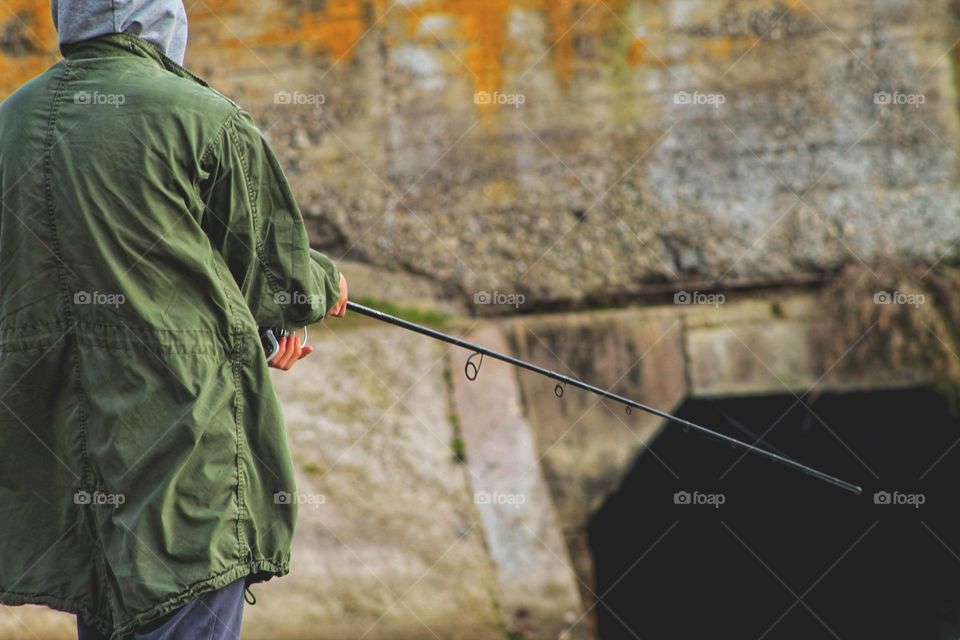 a fisherman in a green cloak holds a spinning rod