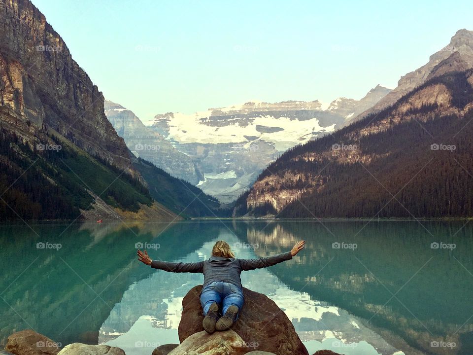 Soaring high as dawn breaks in at beautiful Lake Louise in Banff National Park, Alberta Canada, woman laying on rock arms outstretched as if flying, glacial lake, mountains and reflections, room for text 