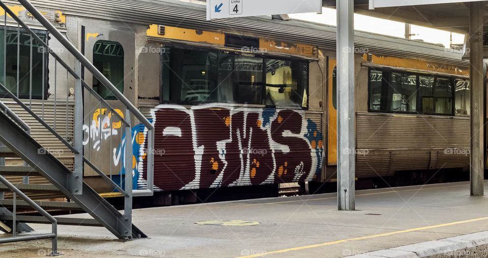 Metal steps and girders of a railway station with a graffitied train at the platform