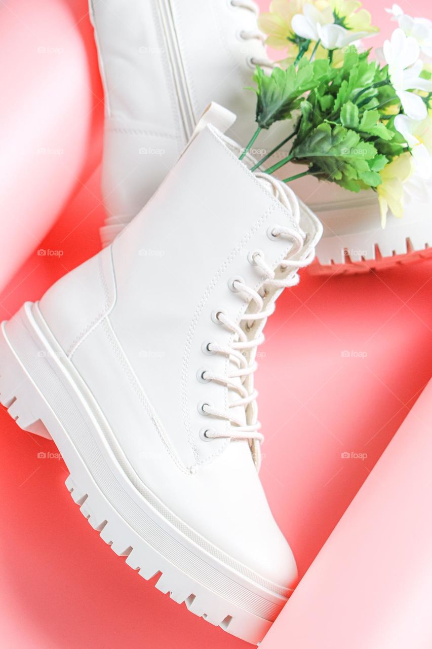 Beautiful white eco leather lace-up shoes with a bouquet of spring faux colors on a one-off background twisted around the edges,side view. The concept of fashionable women's shoes.