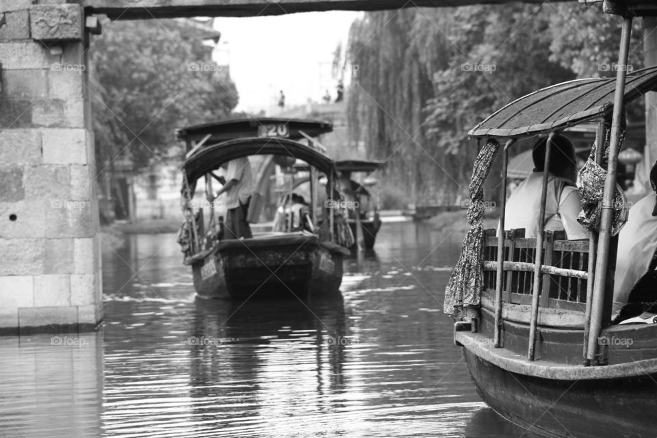 traditional chinese boats, going down a river and underneat a bridge.