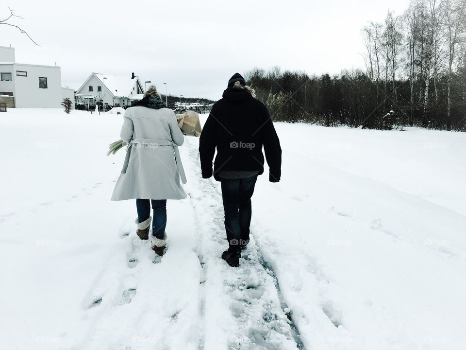 Couple walking in the snow towards their home shown from behind 