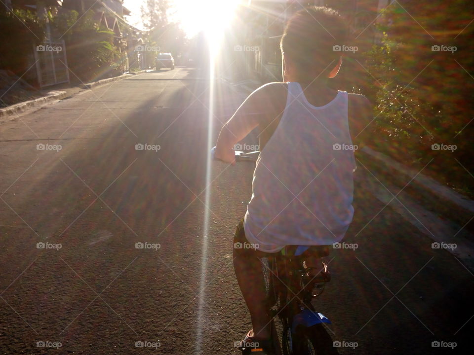 a young boy riding a bicycle towards the sunlight