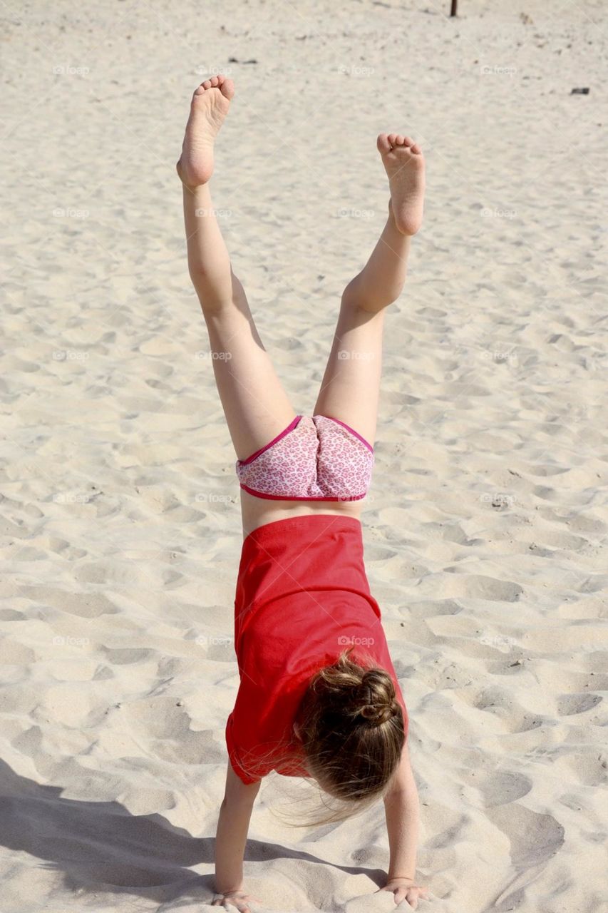 Little girl practicing her handstand on the beach