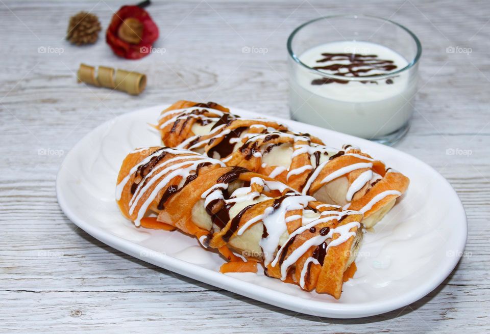 Grid pancakes filed with banana and topped with melted chocolate and sour cream on a white plate