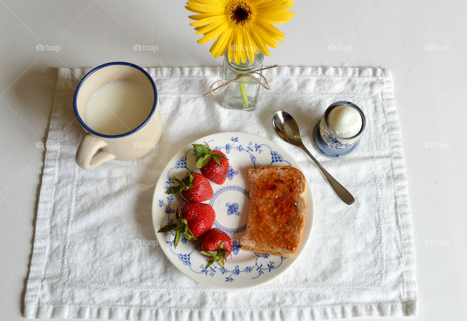 Flat lay of a breakfast of toast, strawberries, egg and milk with a flower