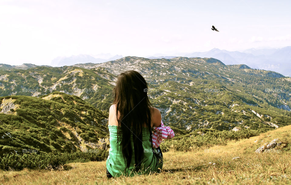 Rear view of a young woman sitting and looking at mountain